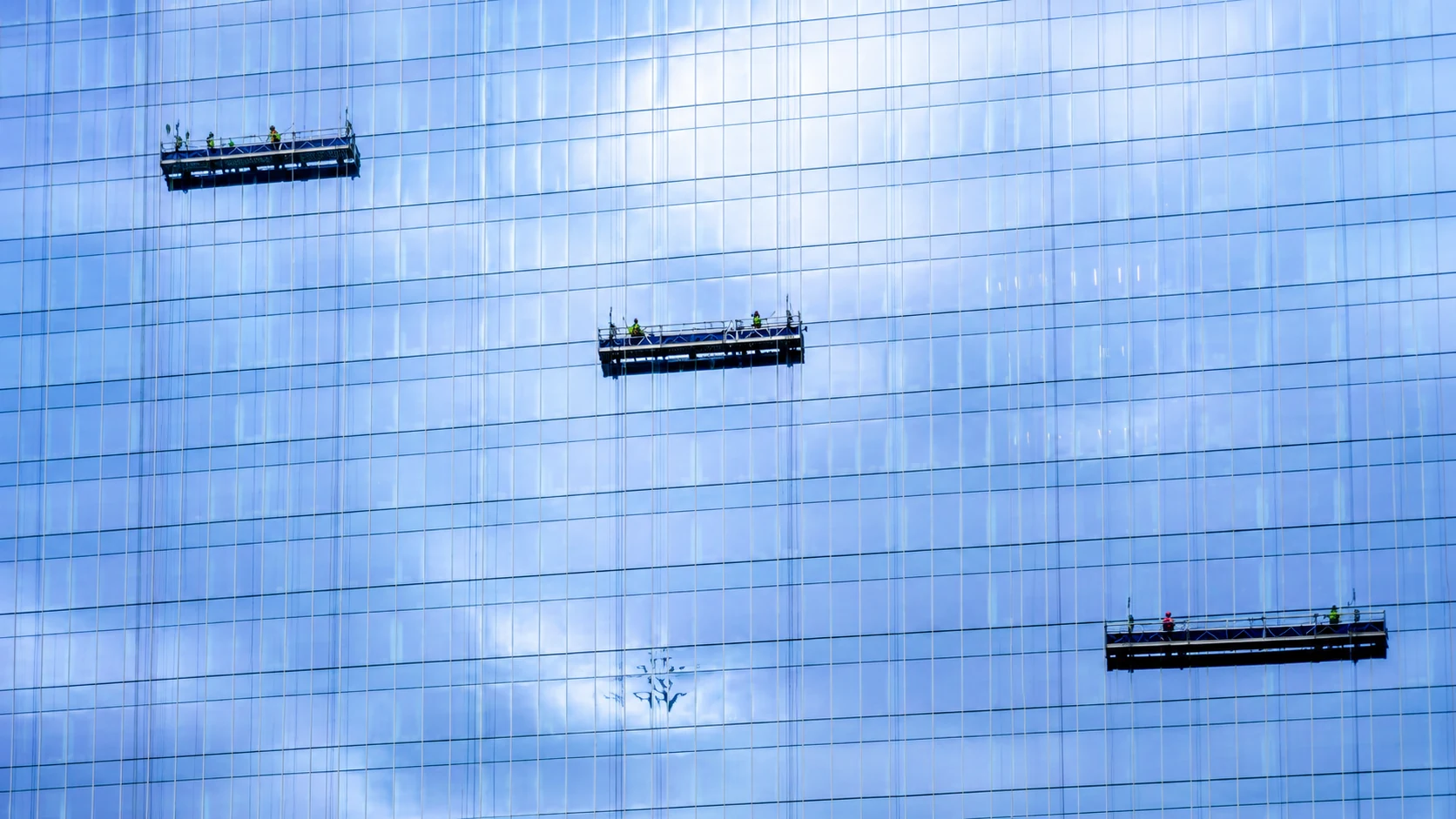 Suspended platforms on a glass building facade.